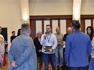 Timo Krasemann – Männerberater für Menschen mit Behinderungen und Deeskalationstrainer im Familienunterstützenden Dienst Steinfurt – ist in Interaktion mit Teilnehmenden. Er hat ein Mikrofon in der Hand und fordert sie auf, anhand konkreter Situationen, kritisch zu reflektieren, ob und in welchem Ausmaß sich seinen Fallbeispielen um Gewalt handelt.